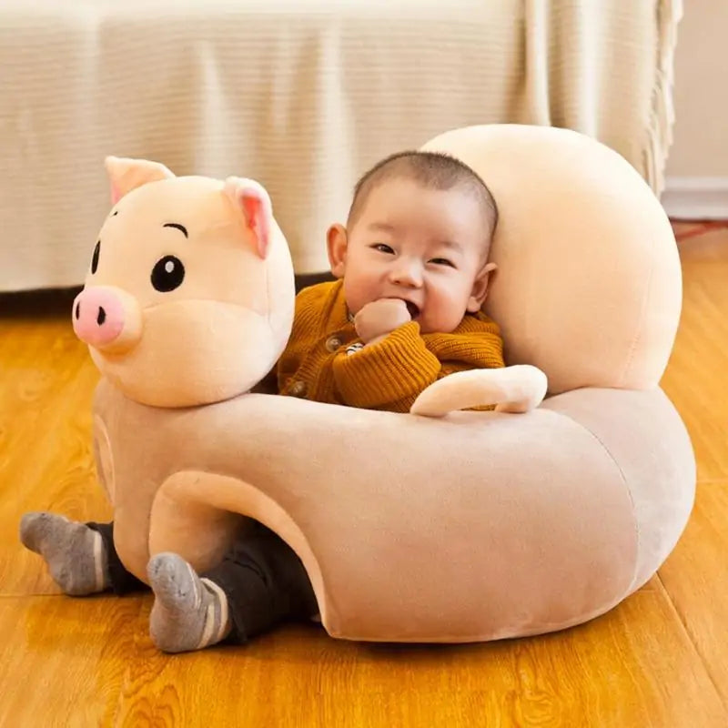 A baby sits comfortably in a plush, Cute Baby Sofa from Gigi & Jade Kids Co., shaped like a pig on a wooden floor. The baby, wearing a brown sweater and gray pants, has a playful expression and rests one hand near their mouth. The light brown chair with its pink snout and big eyes supports cognitive development through ergonomic design.