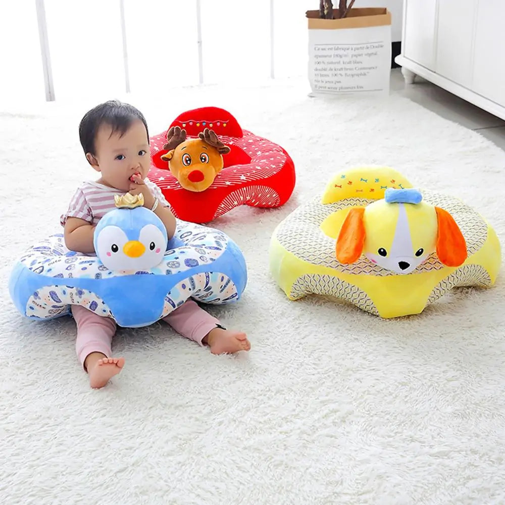 A baby sits in a blue plush Cute Baby Sofa from Gigi & Jade Kids Co., shaped like a penguin, with two other empty seats in the background. One is red with a reindeer design, and the other is yellow with a dog design. The ergonomic design of these seats supports cognitive development, all set on a white, fluffy rug in a brightly lit room.